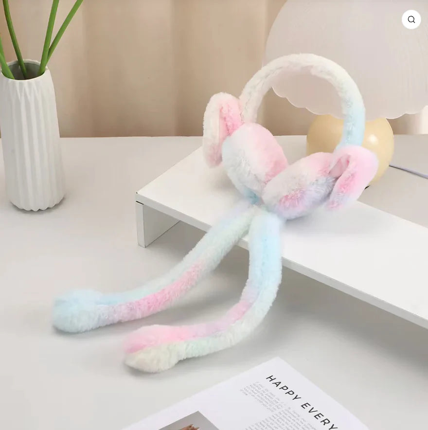 Pastel-colored plush toy on a white surface with a plant and lamp in the background