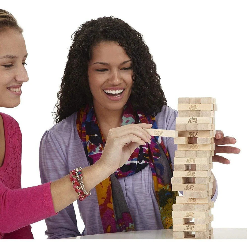 Two women playing with a wooden block tower game on a white background